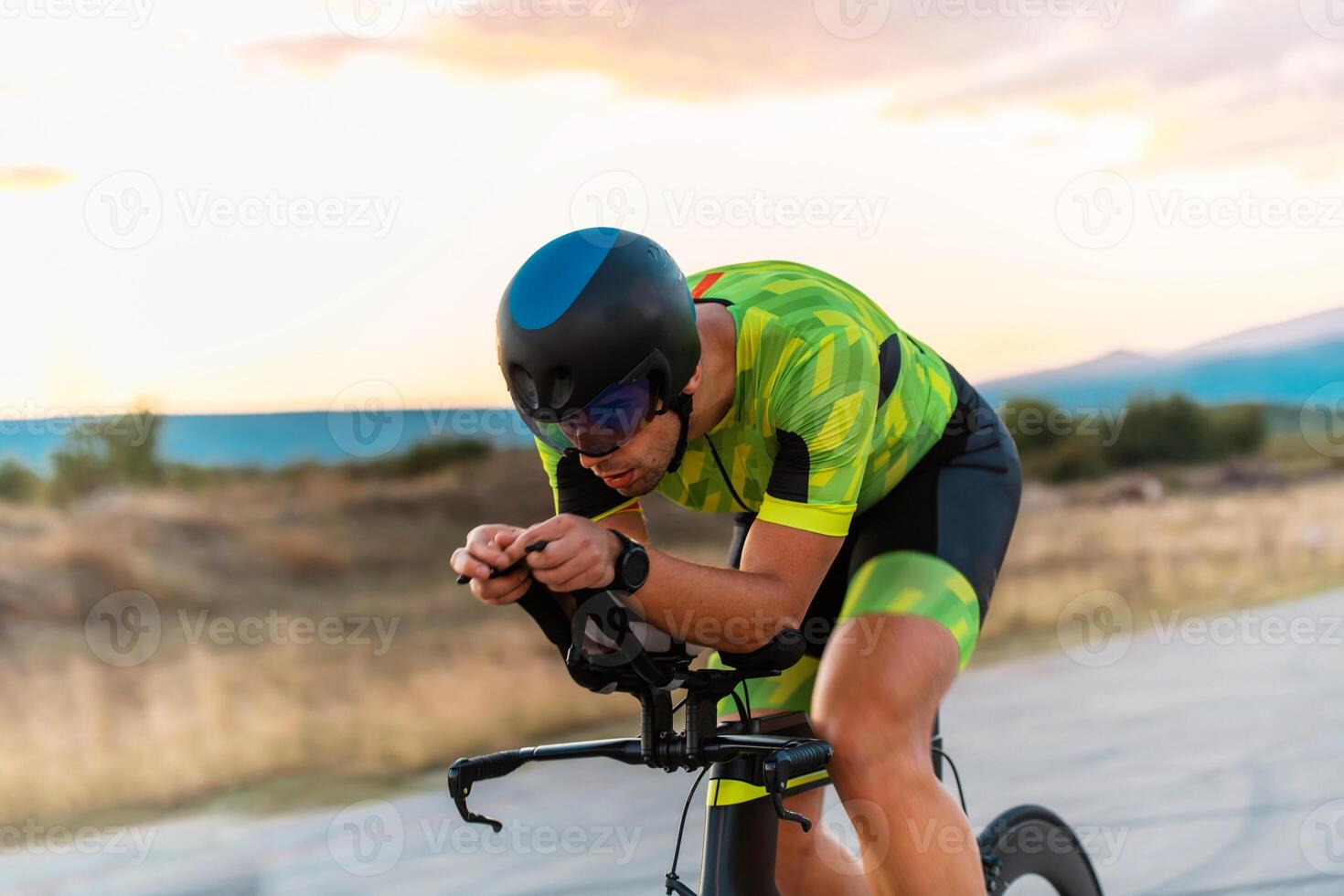 Triathlete riding his bicycle during sunset, preparing for a marathon. The warm colors of the sky provide a beautiful backdrop for his determined and focused effort. photo