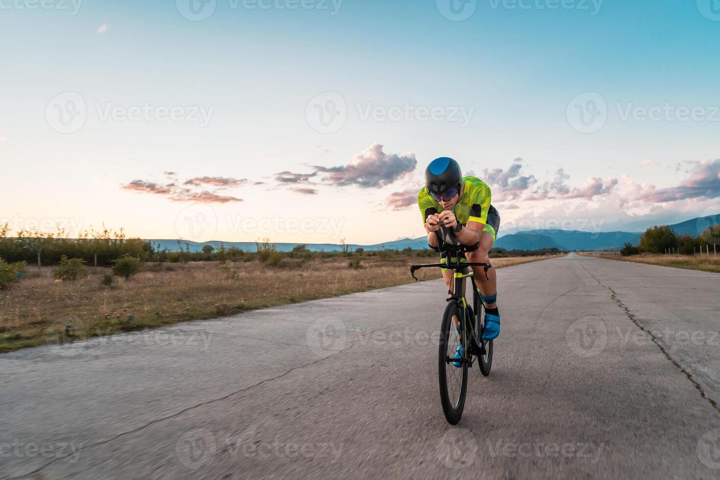 Triathlete riding his bicycle during sunset, preparing for a marathon. The warm colors of the sky provide a beautiful backdrop for his determined and focused effort. photo