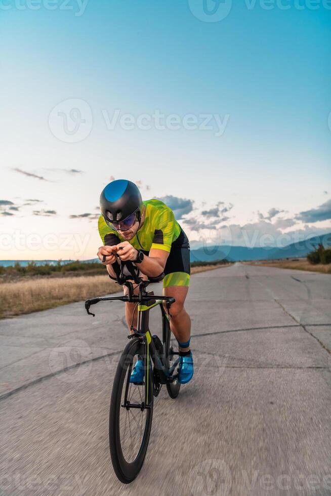 Triathlete riding his bicycle during sunset, preparing for a marathon. The warm colors of the sky provide a beautiful backdrop for his determined and focused effort. photo