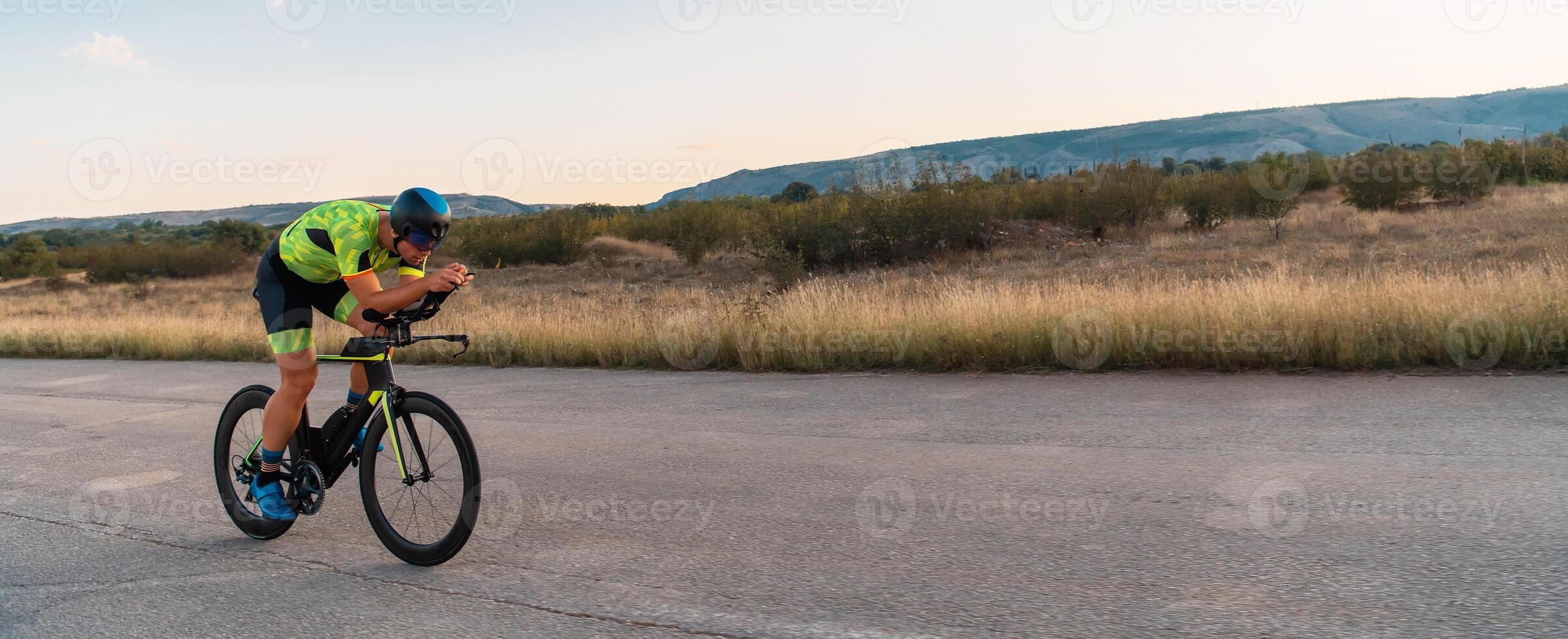 Triathlete riding his bicycle during sunset, preparing for a marathon. The warm colors of the sky provide a beautiful backdrop for his determined and focused effort. photo