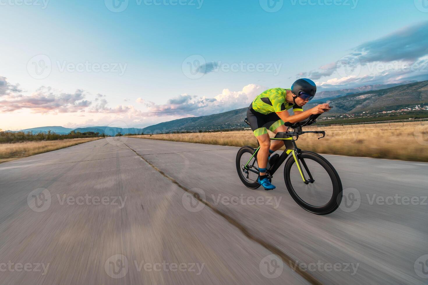Triathlete riding his bicycle during sunset, preparing for a marathon. The warm colors of the sky provide a beautiful backdrop for his determined and focused effort. photo