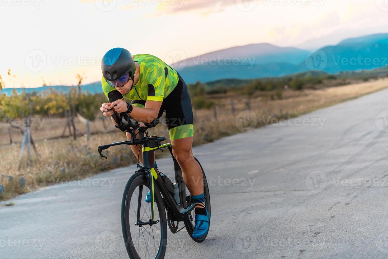 Triathlete riding his bicycle during sunset, preparing for a marathon. The warm colors of the sky provide a beautiful backdrop for his determined and focused effort. photo