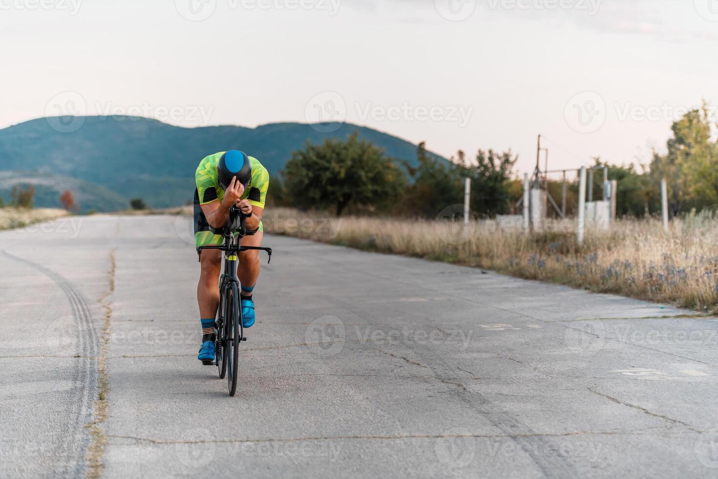 Triathlete riding his bicycle during sunset, preparing for a marathon. The warm colors of the sky provide a beautiful backdrop for his determined and focused effort. photo