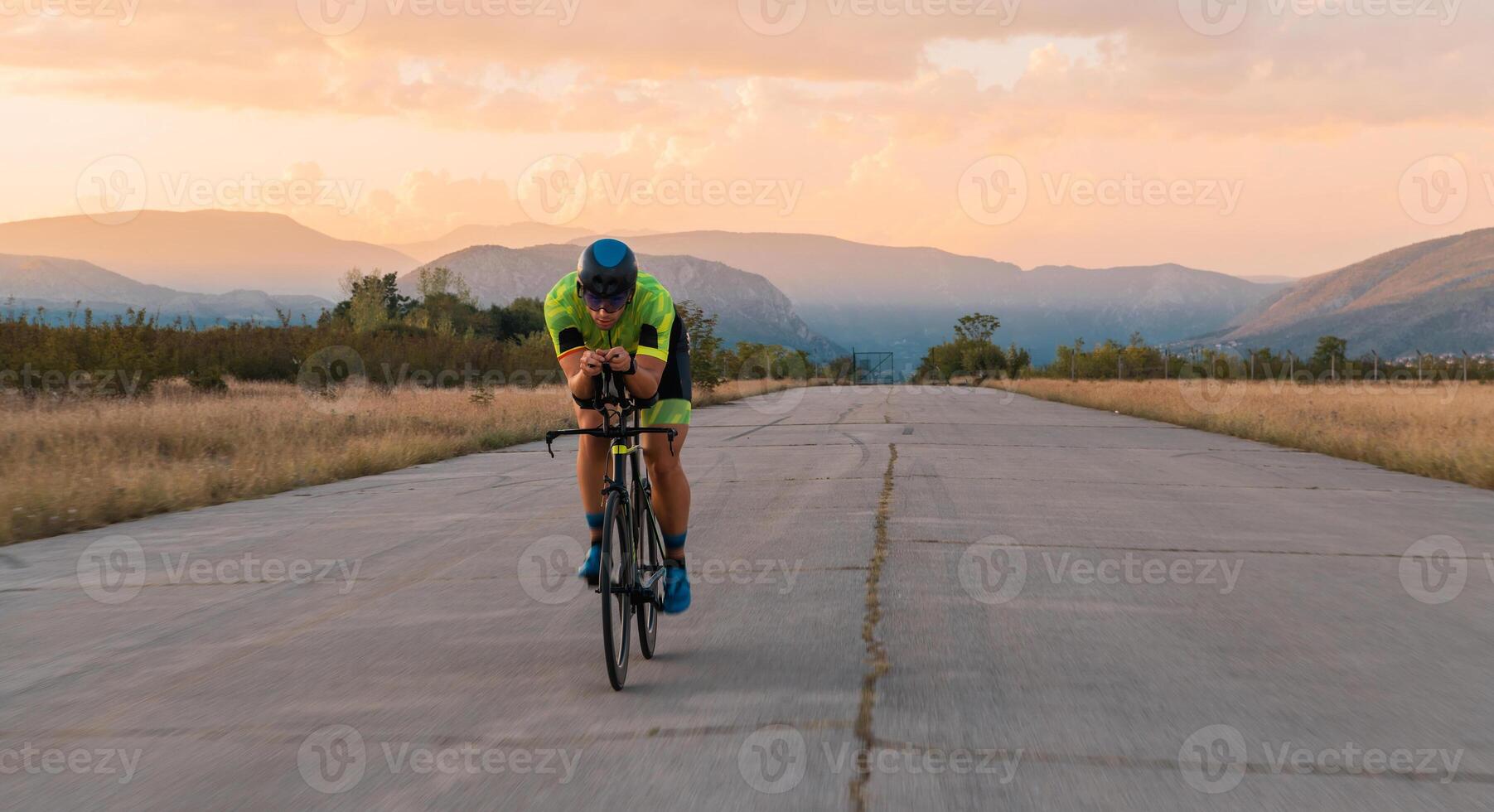 Triathlete riding his bicycle during sunset, preparing for a marathon. The warm colors of the sky provide a beautiful backdrop for his determined and focused effort. photo