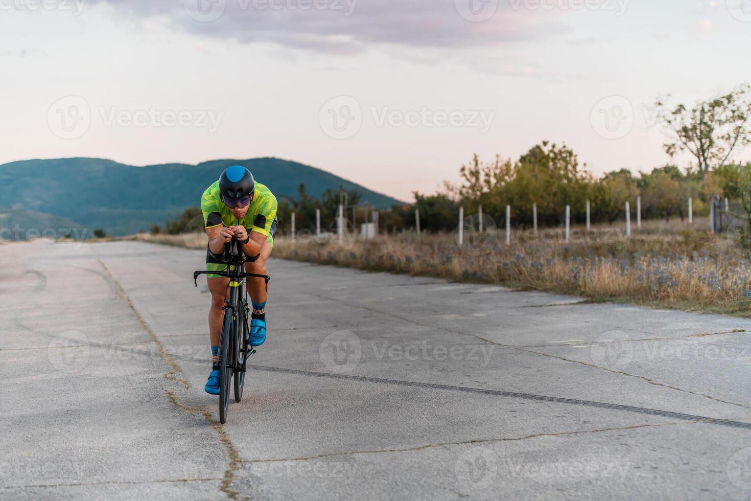 Triathlete riding his bicycle during sunset, preparing for a marathon. The warm colors of the sky provide a beautiful backdrop for his determined and focused effort. photo