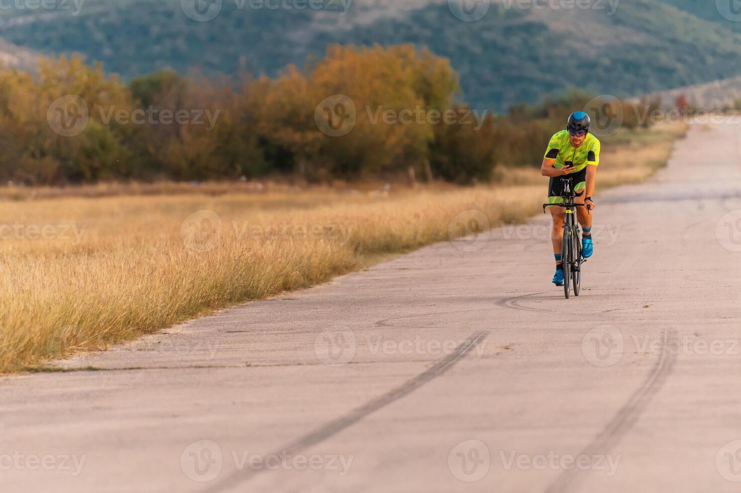 Triathlete riding his bicycle during sunset, preparing for a marathon. The warm colors of the sky provide a beautiful backdrop for his determined and focused effort. photo