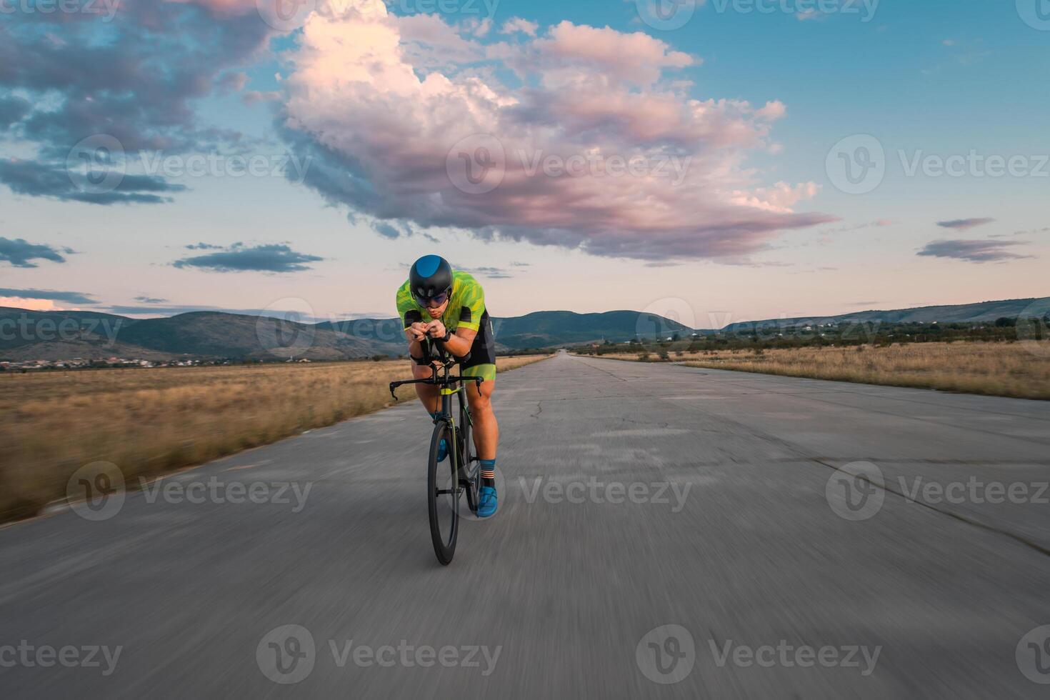 Triathlete riding his bicycle during sunset, preparing for a marathon. The warm colors of the sky provide a beautiful backdrop for his determined and focused effort. photo