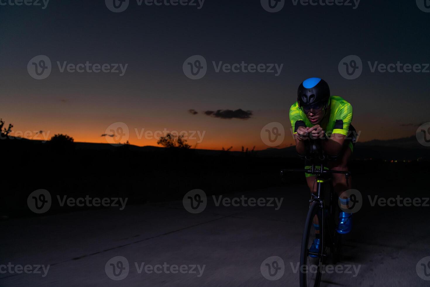 A triathlete rides his bike in the darkness of night, pushing himself to prepare for a marathon. The contrast between the darkness and the light of his bike creates a sense of drama and highlights the photo