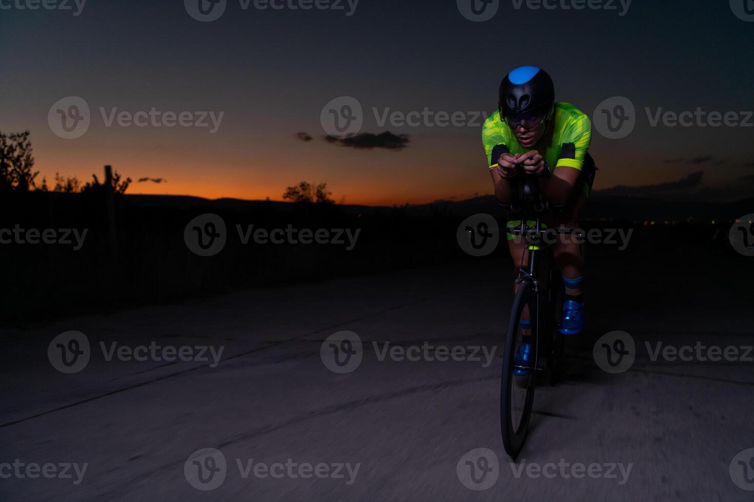A triathlete rides his bike in the darkness of night, pushing himself to prepare for a marathon. The contrast between the darkness and the light of his bike creates a sense of drama and highlights the photo