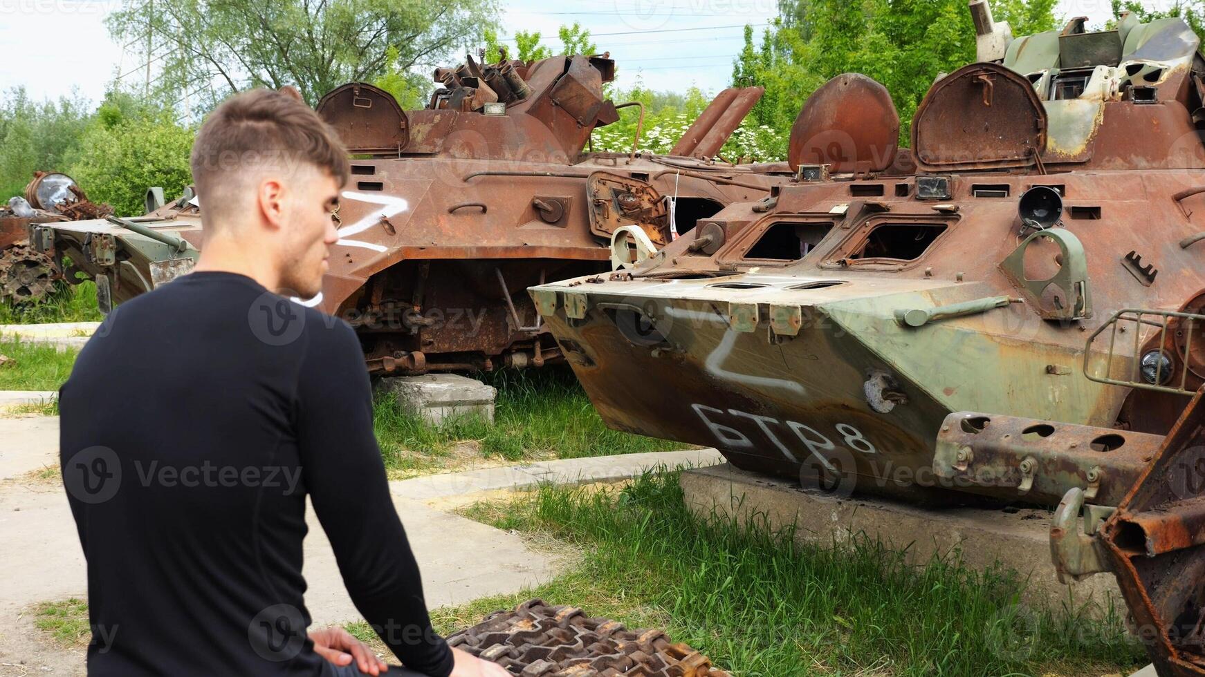 Young man looking at destroyed military equipment of the russian army. Exhibition of rusty and burned-out armored vehicles on ukrainian territory. War between Ukraine and russia. Slow mo photo
