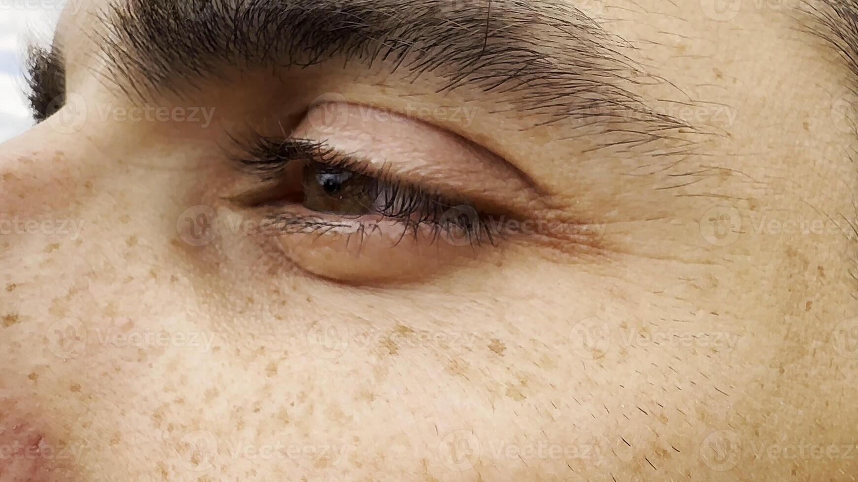 Focus on left brown eye of handsome sorrowful man looking into the distance. Portrait of unhappy male face with freckles outdoor. Upset facial expression of young guy. Close up photo