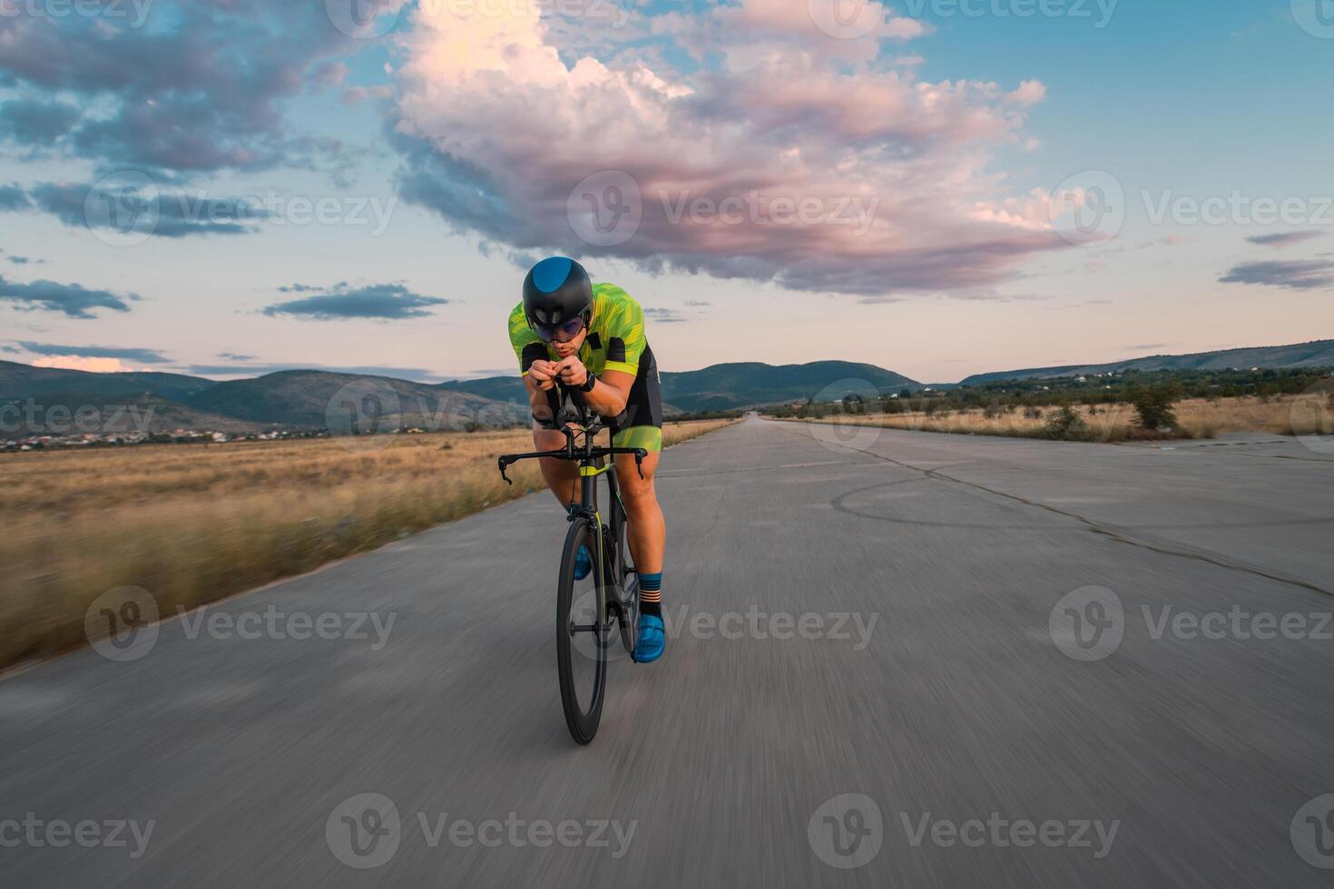 Triathlete riding his bicycle during sunset, preparing for a marathon. The warm colors of the sky provide a beautiful backdrop for his determined and focused effort. photo
