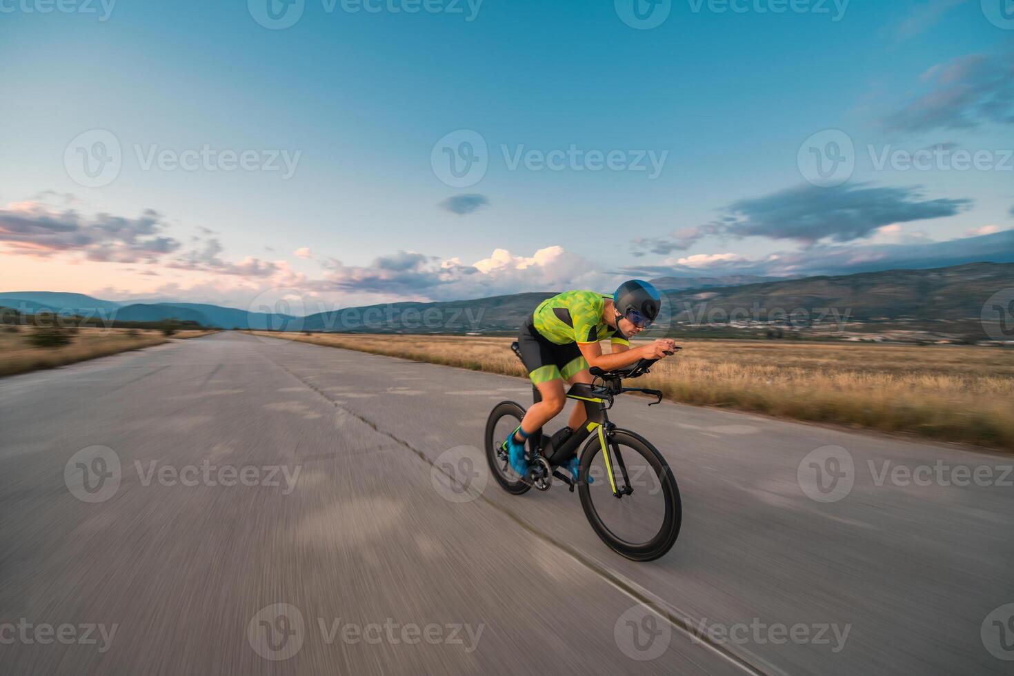Triathlete riding his bicycle during sunset, preparing for a marathon. The warm colors of the sky provide a beautiful backdrop for his determined and focused effort. photo