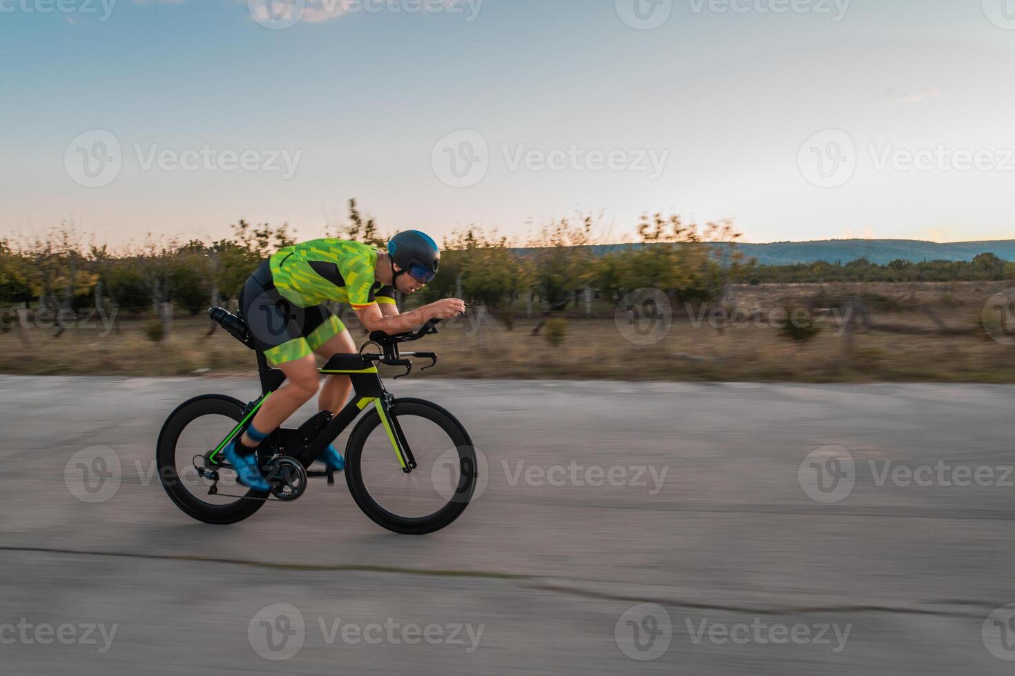 Triathlete riding his bicycle during sunset, preparing for a marathon. The warm colors of the sky provide a beautiful backdrop for his determined and focused effort. photo