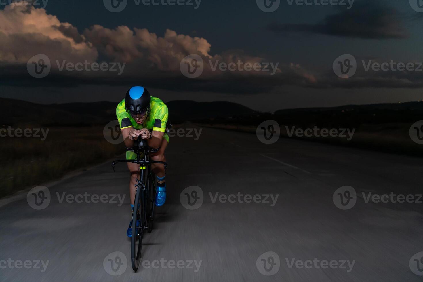A triathlete rides his bike in the darkness of night, pushing himself to prepare for a marathon. The contrast between the darkness and the light of his bike creates a sense of drama and highlights the photo