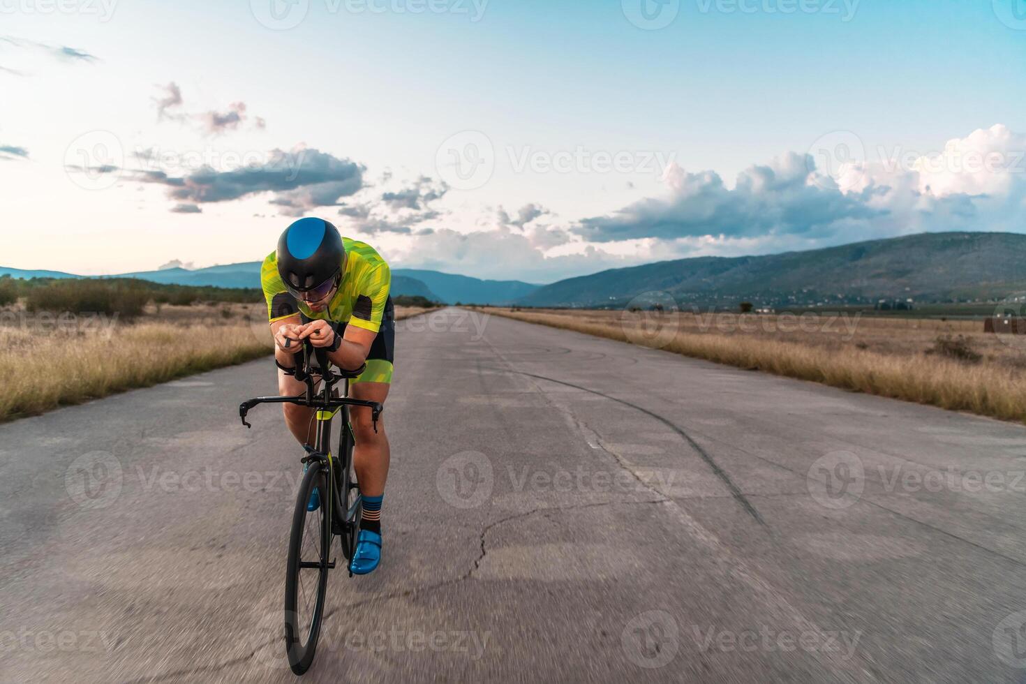 Triathlete riding his bicycle during sunset, preparing for a marathon. The warm colors of the sky provide a beautiful backdrop for his determined and focused effort. photo
