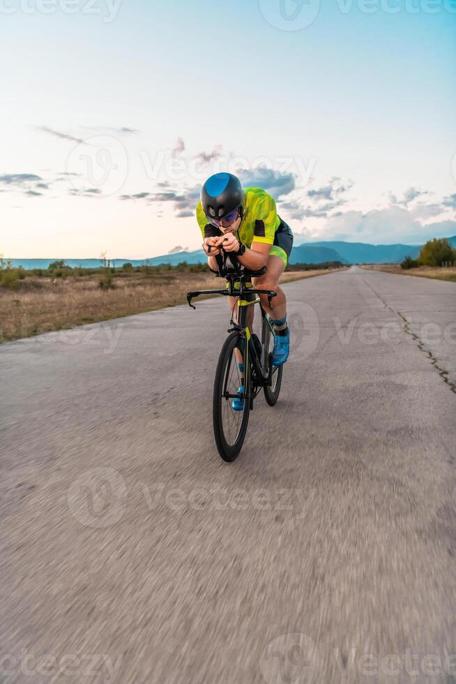 Triathlete riding his bicycle during sunset, preparing for a marathon. The warm colors of the sky provide a beautiful backdrop for his determined and focused effort. photo