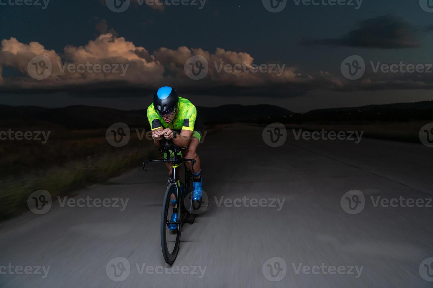 A triathlete rides his bike in the darkness of night, pushing himself to prepare for a marathon. The contrast between the darkness and the light of his bike creates a sense of drama and highlights the photo