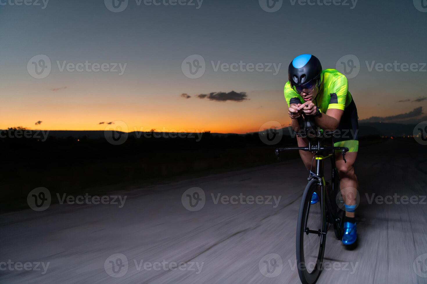 A triathlete rides his bike in the darkness of night, pushing himself to prepare for a marathon. The contrast between the darkness and the light of his bike creates a sense of drama and highlights the photo