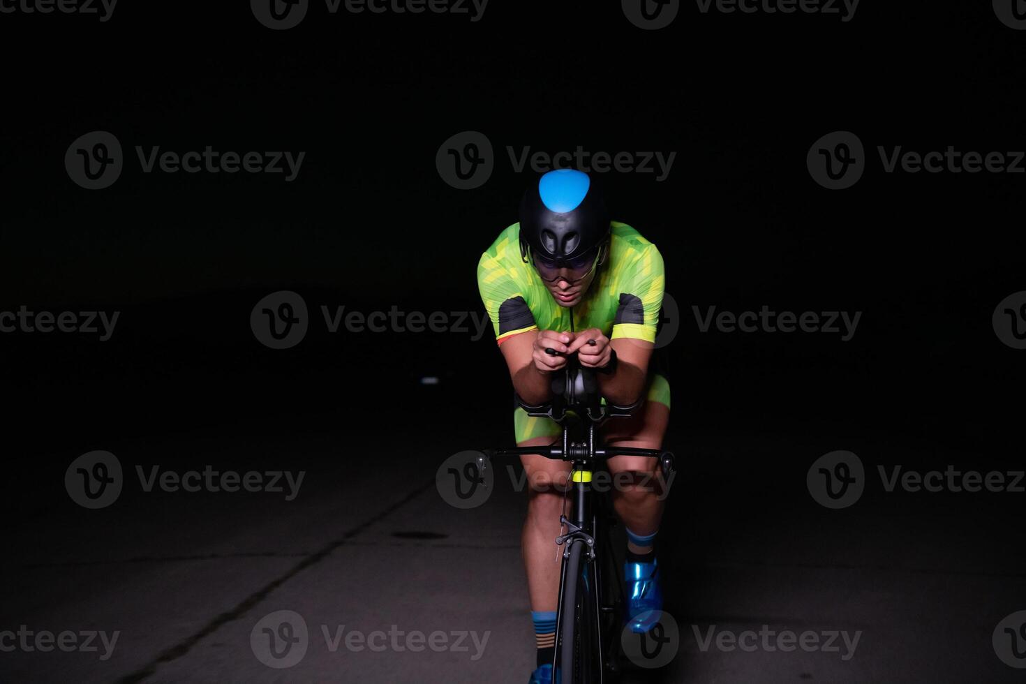 A triathlete rides his bike in the darkness of night, pushing himself to prepare for a marathon. The contrast between the darkness and the light of his bike creates a sense of drama and highlights the photo