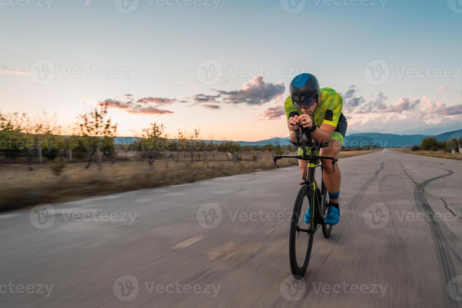 Triathlete riding his bicycle during sunset, preparing for a marathon. The warm colors of the sky provide a beautiful backdrop for his determined and focused effort. photo