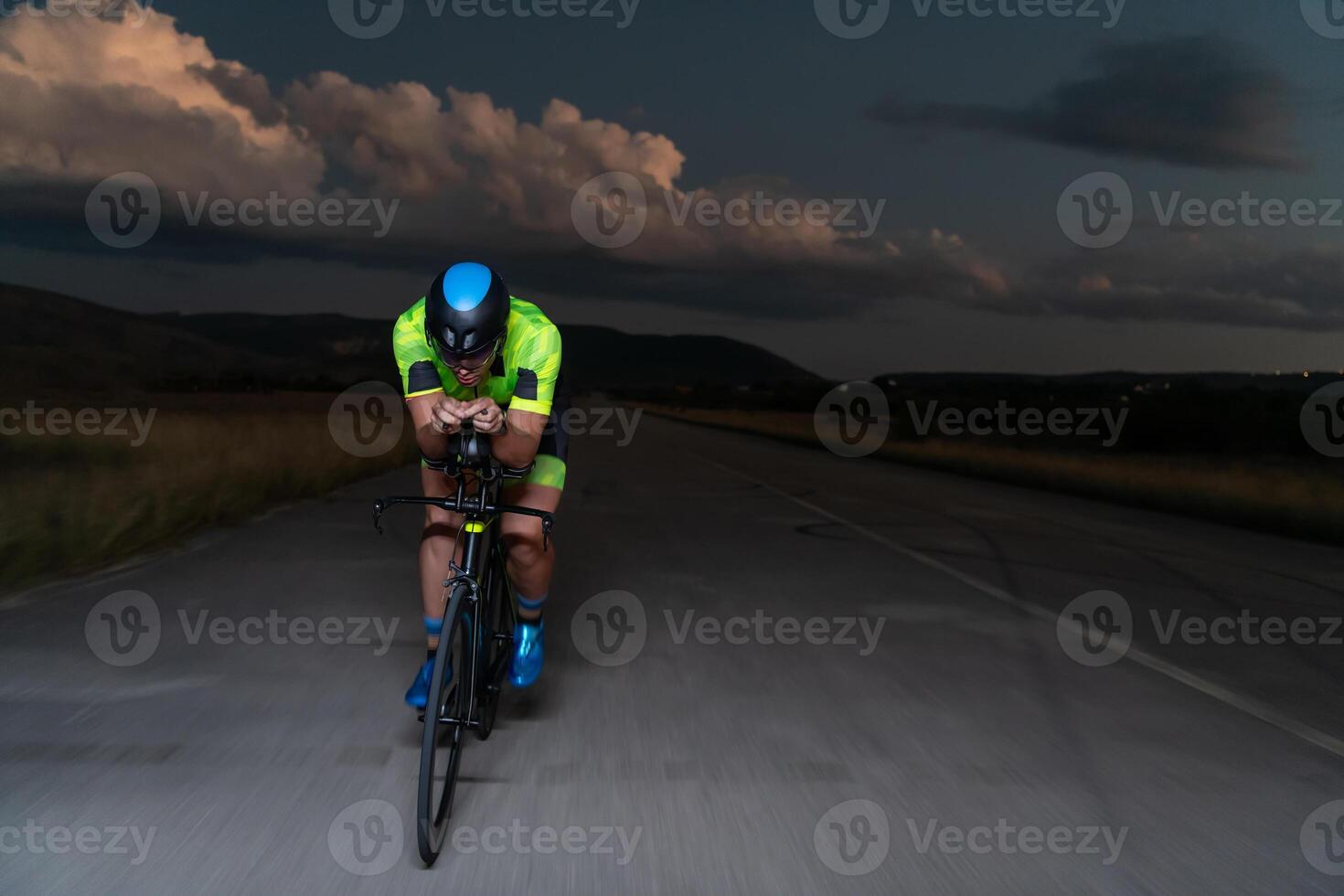 A triathlete rides his bike in the darkness of night, pushing himself to prepare for a marathon. The contrast between the darkness and the light of his bike creates a sense of drama and highlights the photo