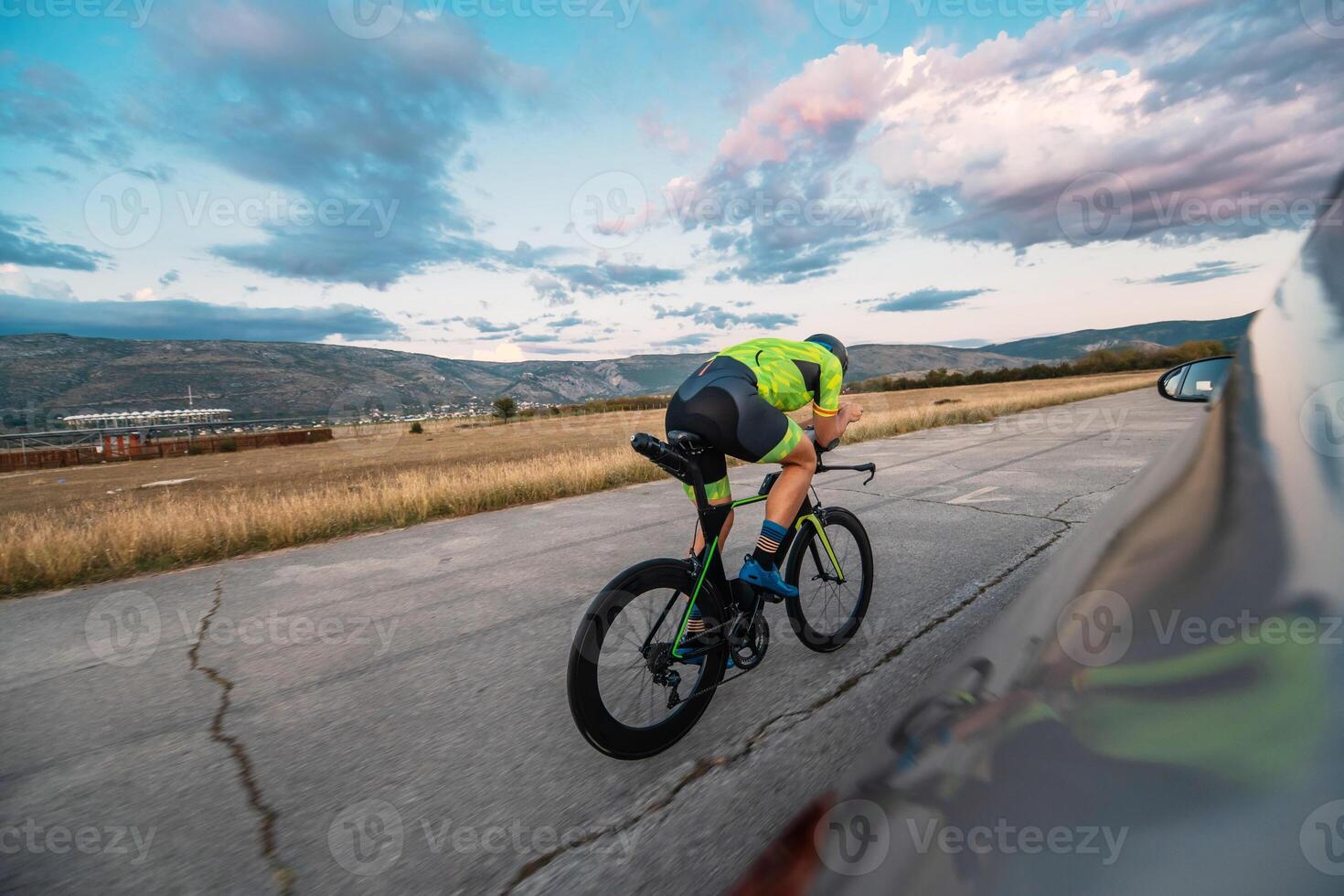 Triathlete riding his bicycle during sunset, preparing for a marathon. The warm colors of the sky provide a beautiful backdrop for his determined and focused effort. photo