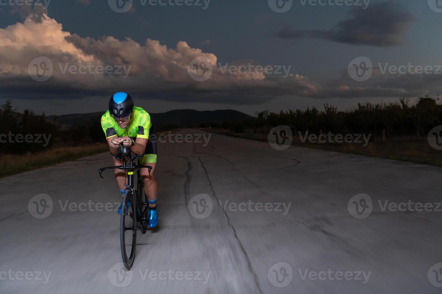 A triathlete rides his bike in the darkness of night, pushing himself to prepare for a marathon. The contrast between the darkness and the light of his bike creates a sense of drama and highlights the photo