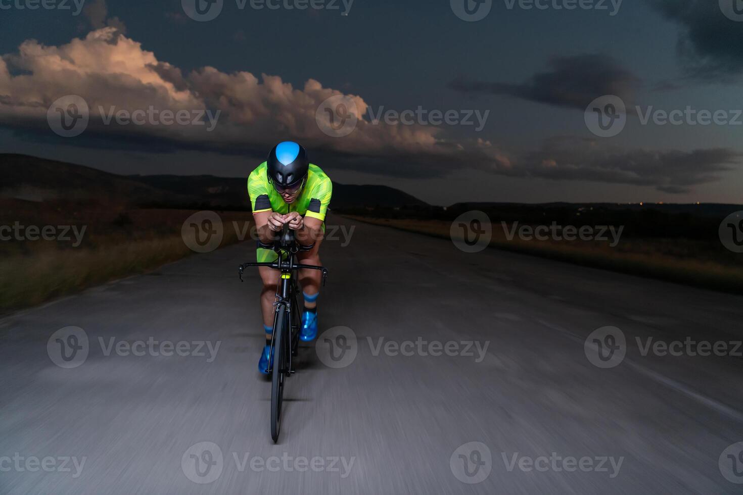 A triathlete rides his bike in the darkness of night, pushing himself to prepare for a marathon. The contrast between the darkness and the light of his bike creates a sense of drama and highlights the photo
