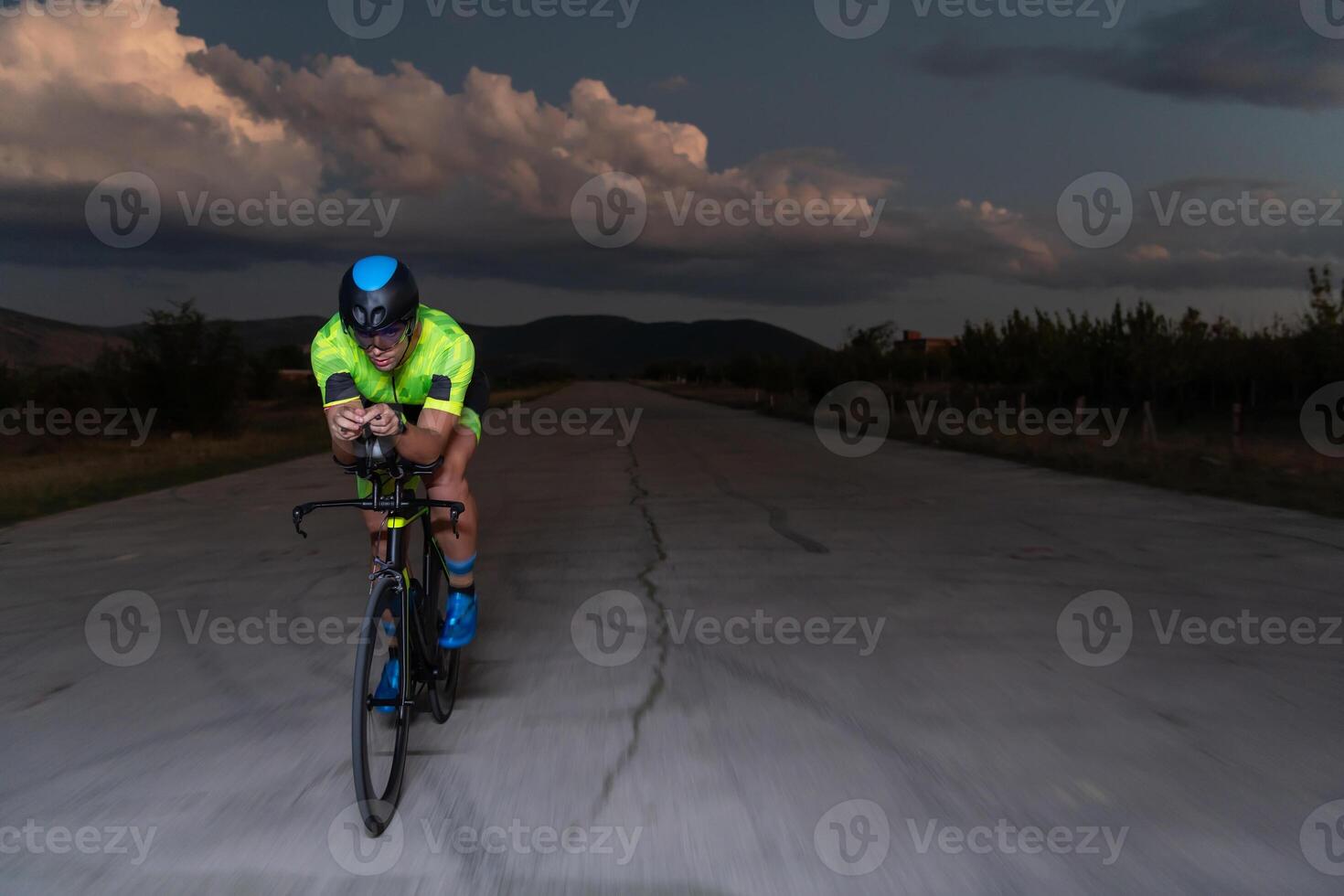 A triathlete rides his bike in the darkness of night, pushing himself to prepare for a marathon. The contrast between the darkness and the light of his bike creates a sense of drama and highlights the photo