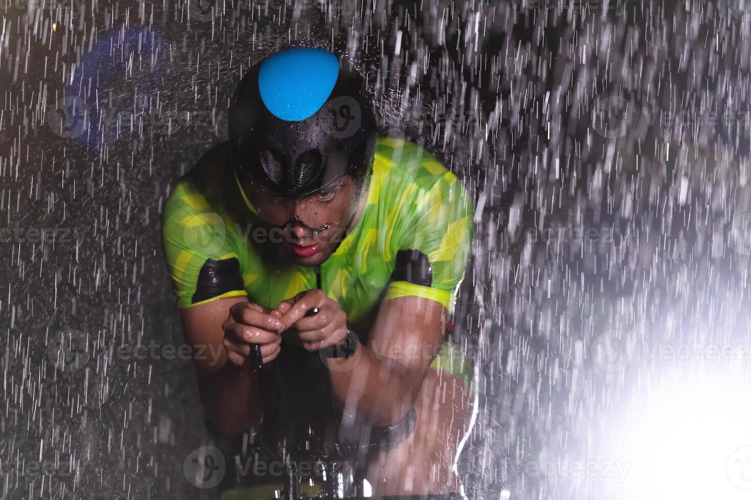 A triathlete braving the rain as he cycles through the night, preparing himself for the upcoming marathon photo