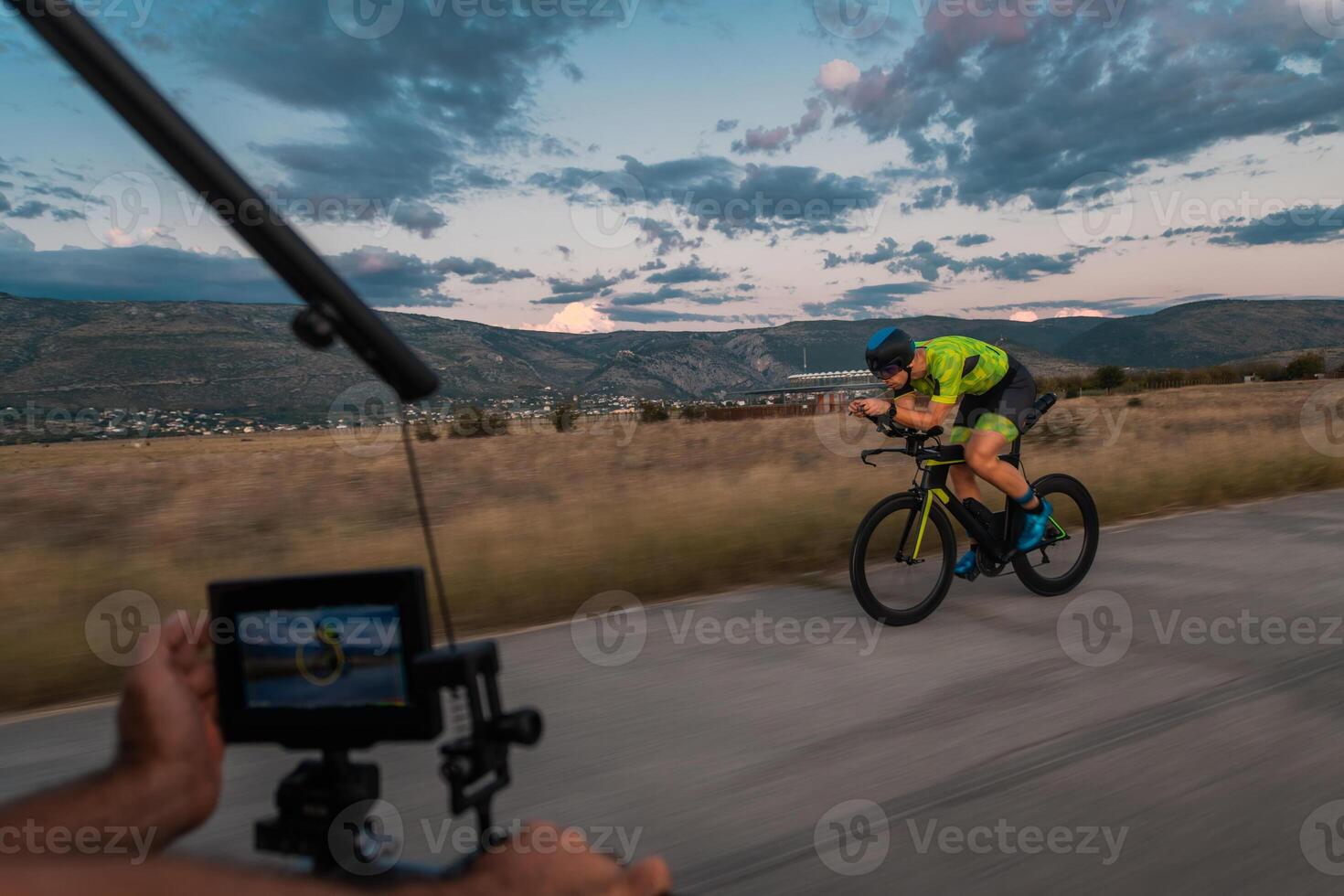 A videographer recording a triathlete riding his bike preparing for an upcoming marathon.Athlete's physical endurance and the dedication required to succeed in the sport. photo