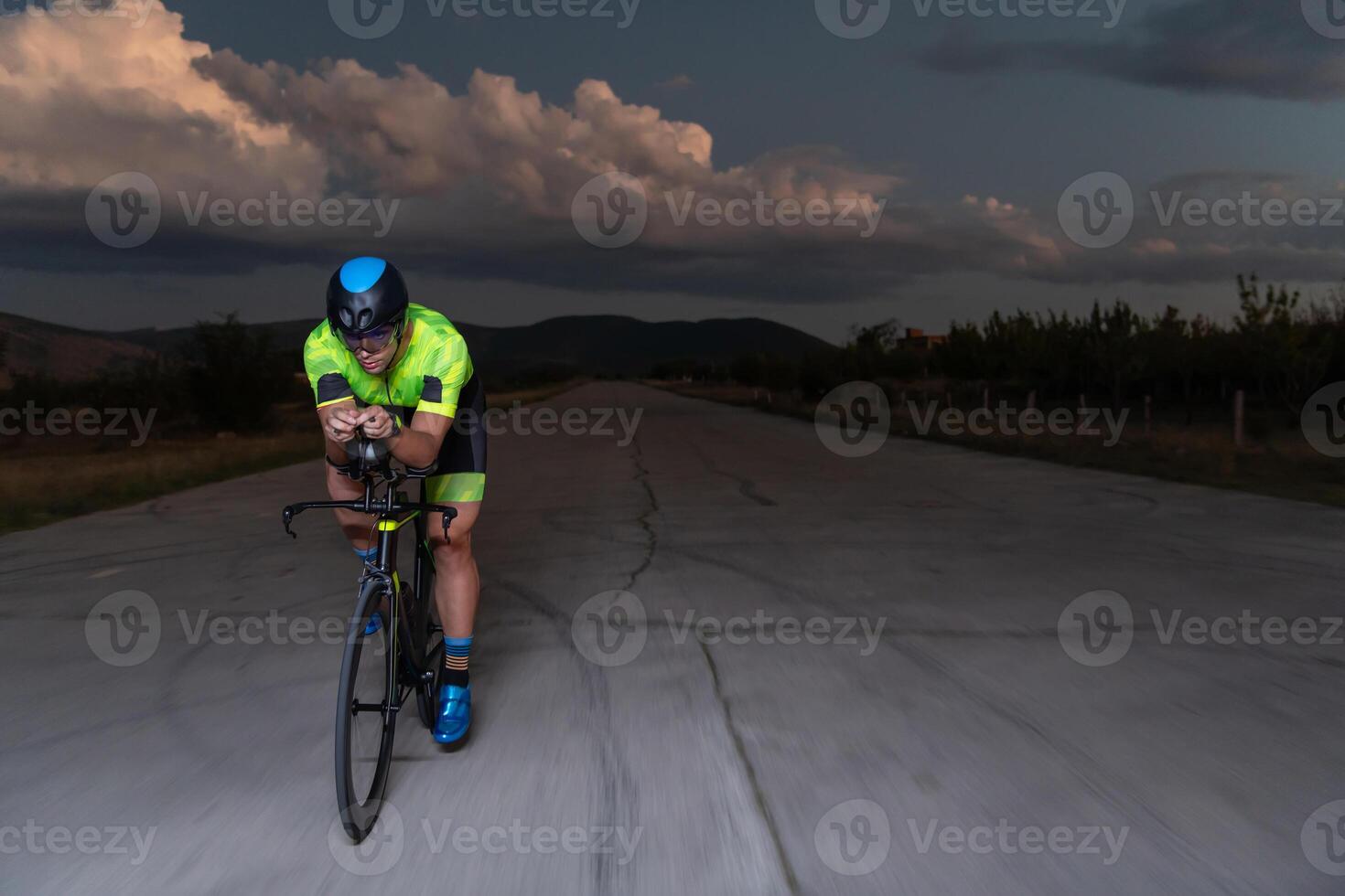 A triathlete rides his bike in the darkness of night, pushing himself to prepare for a marathon. The contrast between the darkness and the light of his bike creates a sense of drama and highlights the photo