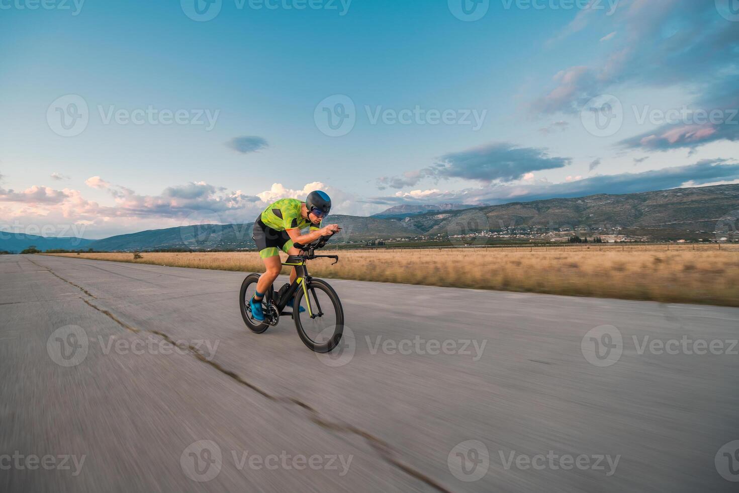 Triathlete riding his bicycle during sunset, preparing for a marathon. The warm colors of the sky provide a beautiful backdrop for his determined and focused effort. photo