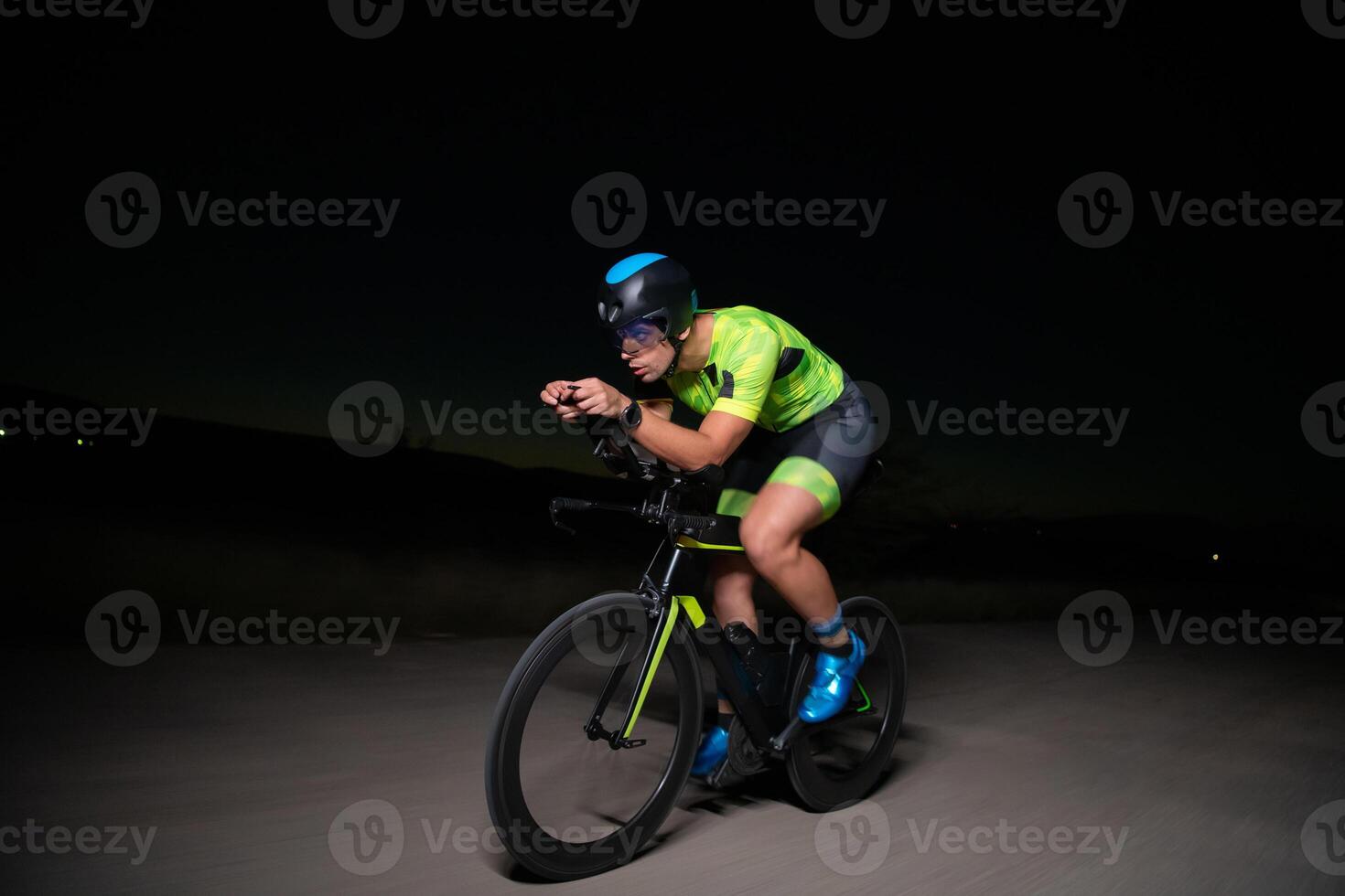 A triathlete rides his bike in the darkness of night, pushing himself to prepare for a marathon. The contrast between the darkness and the light of his bike creates a sense of drama and highlights the photo