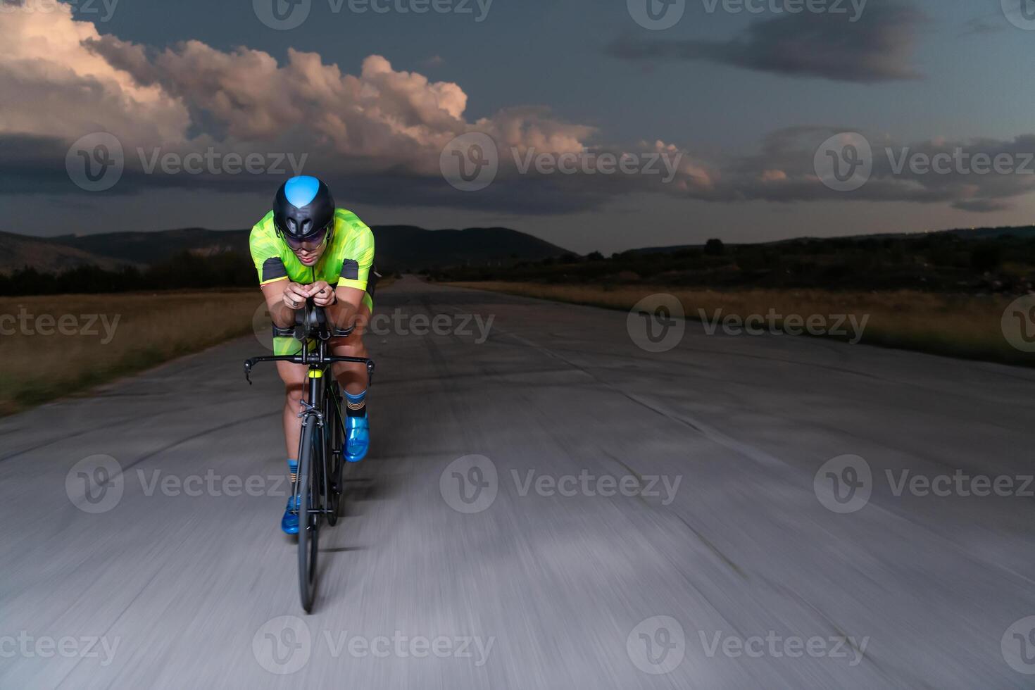A triathlete rides his bike in the darkness of night, pushing himself to prepare for a marathon. The contrast between the darkness and the light of his bike creates a sense of drama and highlights the photo