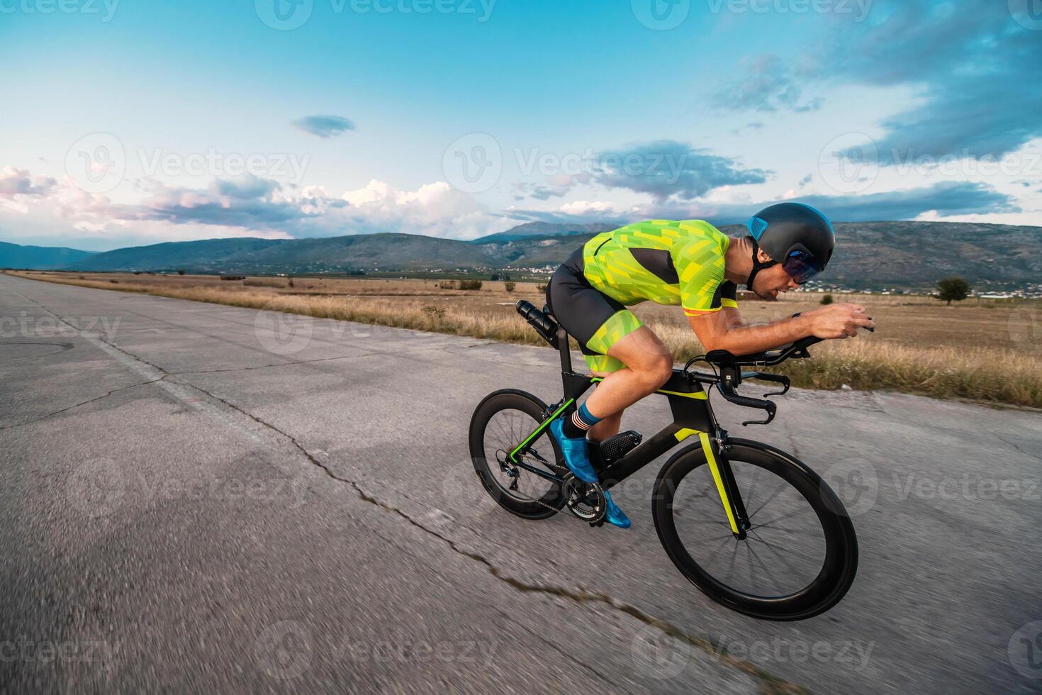 Triathlete riding his bicycle during sunset, preparing for a marathon. The warm colors of the sky provide a beautiful backdrop for his determined and focused effort. photo