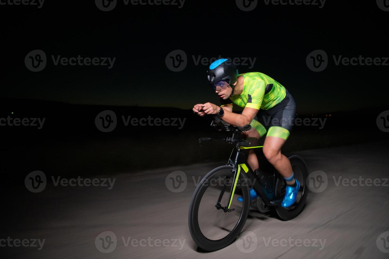 A triathlete rides his bike in the darkness of night, pushing himself to prepare for a marathon. The contrast between the darkness and the light of his bike creates a sense of drama and highlights the photo