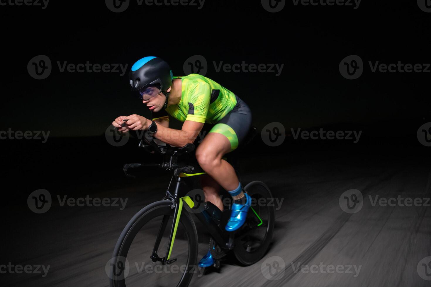 A triathlete rides his bike in the darkness of night, pushing himself to prepare for a marathon. The contrast between the darkness and the light of his bike creates a sense of drama and highlights the photo