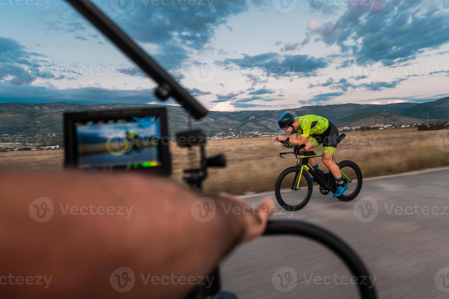A videographer recording a triathlete riding his bike preparing for an upcoming marathon.Athlete's physical endurance and the dedication required to succeed in the sport. photo