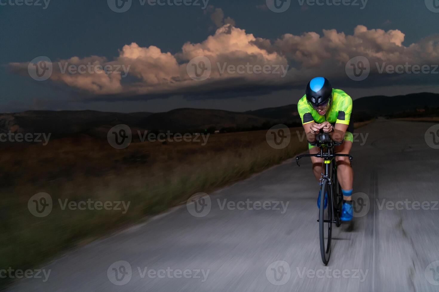 A triathlete rides his bike in the darkness of night, pushing himself to prepare for a marathon. The contrast between the darkness and the light of his bike creates a sense of drama and highlights the photo