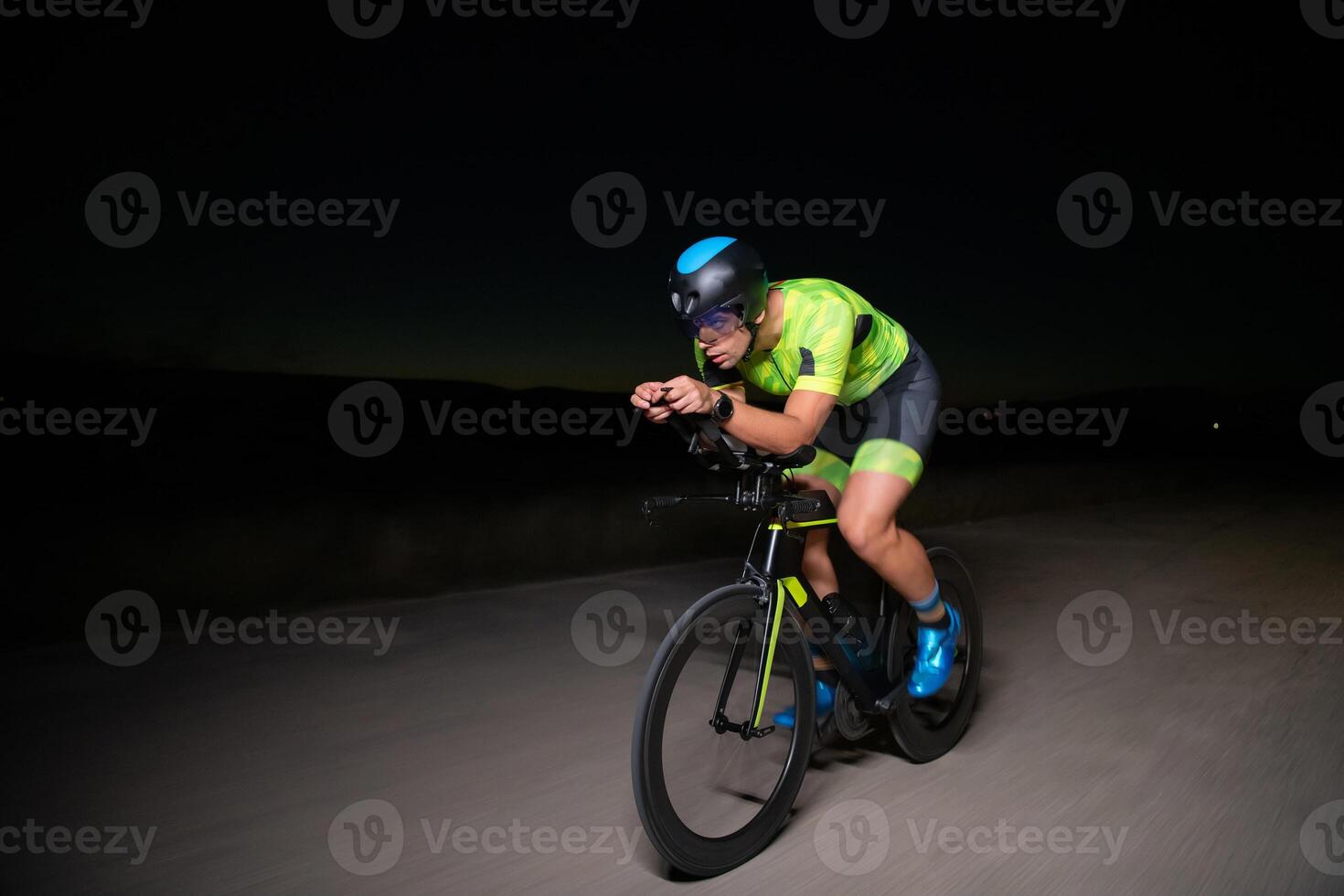 A triathlete rides his bike in the darkness of night, pushing himself to prepare for a marathon. The contrast between the darkness and the light of his bike creates a sense of drama and highlights the photo
