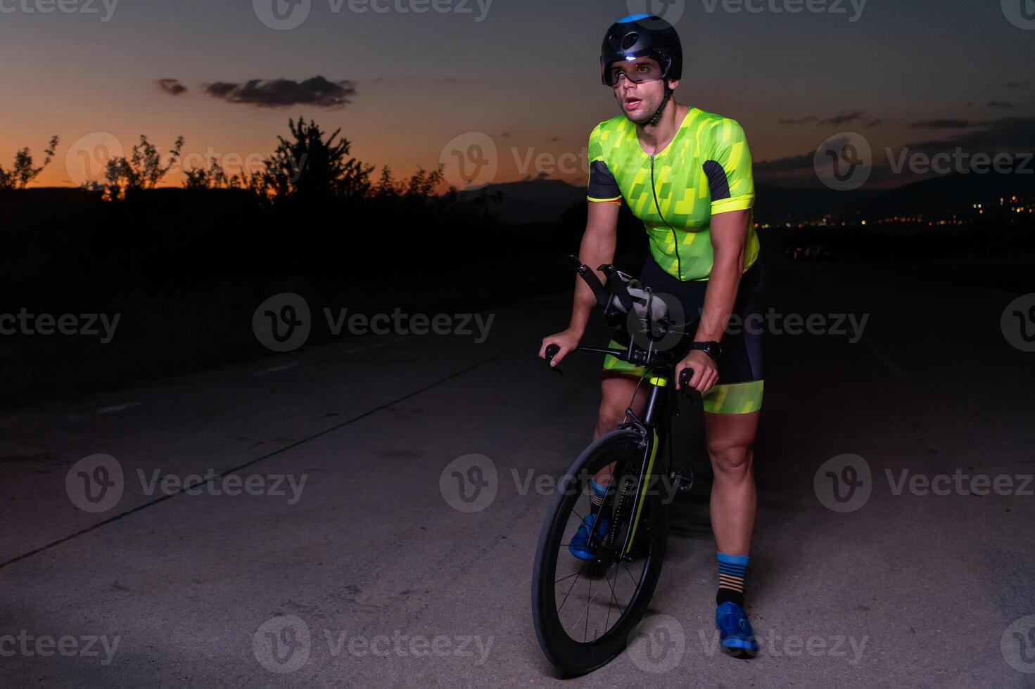 A triathlete rides his bike in the darkness of night, pushing himself to prepare for a marathon. The contrast between the darkness and the light of his bike creates a sense of drama and highlights the photo