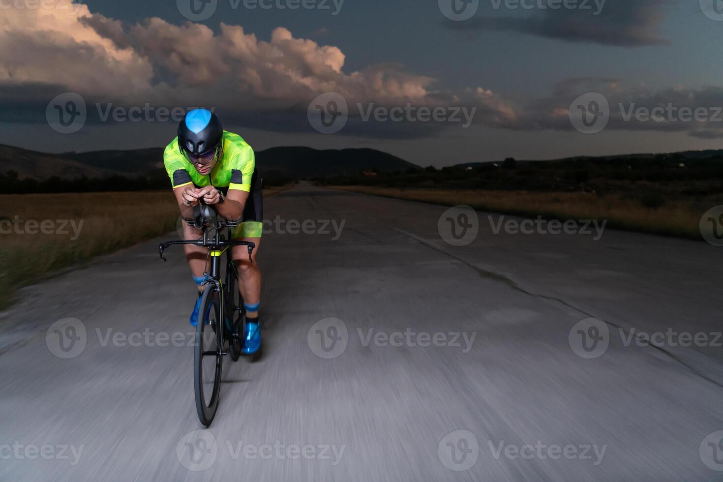A triathlete rides his bike in the darkness of night, pushing himself to prepare for a marathon. The contrast between the darkness and the light of his bike creates a sense of drama and highlights the photo