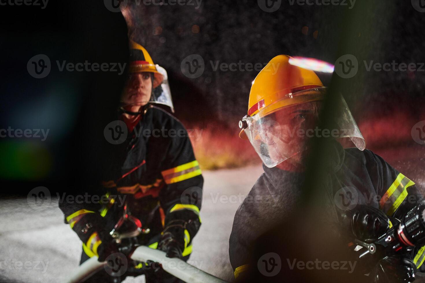 Firefighters using a water hose to eliminate a fire hazard. Team of female and male firemen in dangerous rescue mission. photo