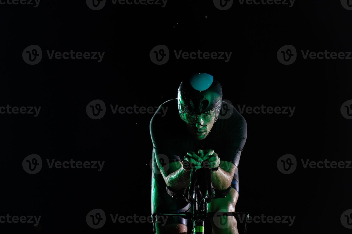 A triathlete rides his bike in the darkness of night, pushing himself to prepare for a marathon. The contrast between the darkness and the light of his bike creates a sense of drama and highlights the photo