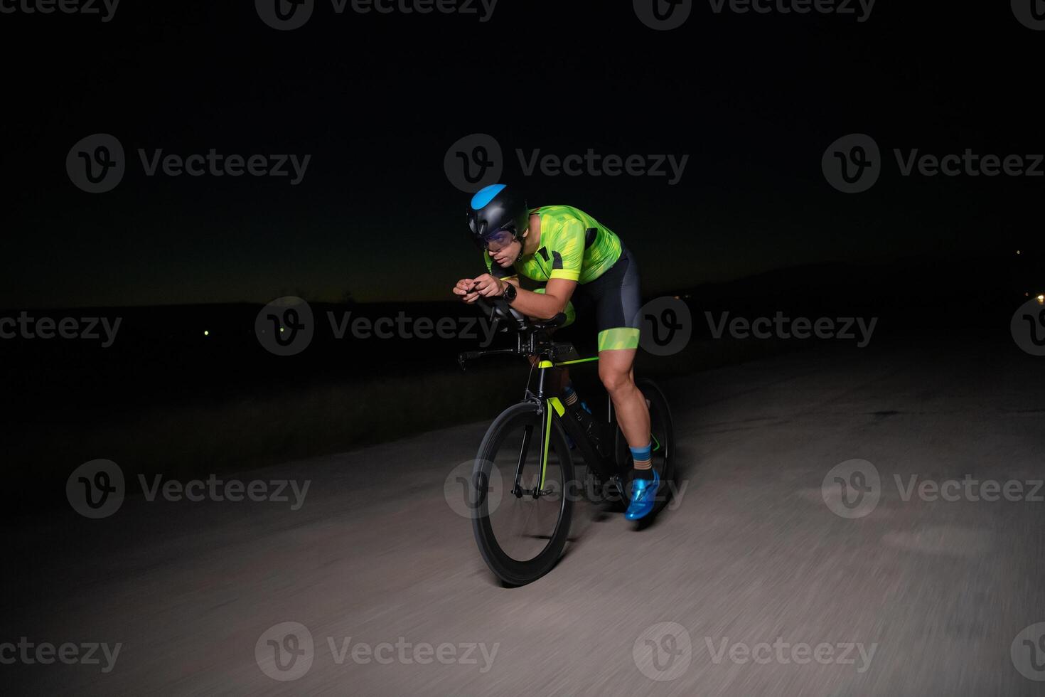 A triathlete rides his bike in the darkness of night, pushing himself to prepare for a marathon. The contrast between the darkness and the light of his bike creates a sense of drama and highlights the photo