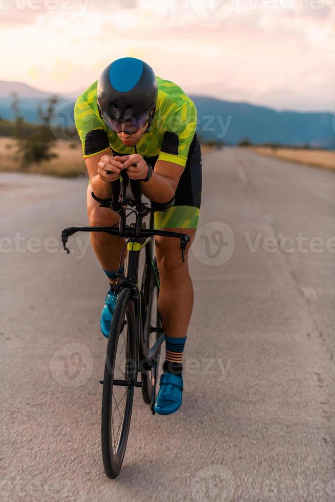 Triathlete riding his bicycle during sunset, preparing for a marathon. The warm colors of the sky provide a beautiful backdrop for his determined and focused effort. photo