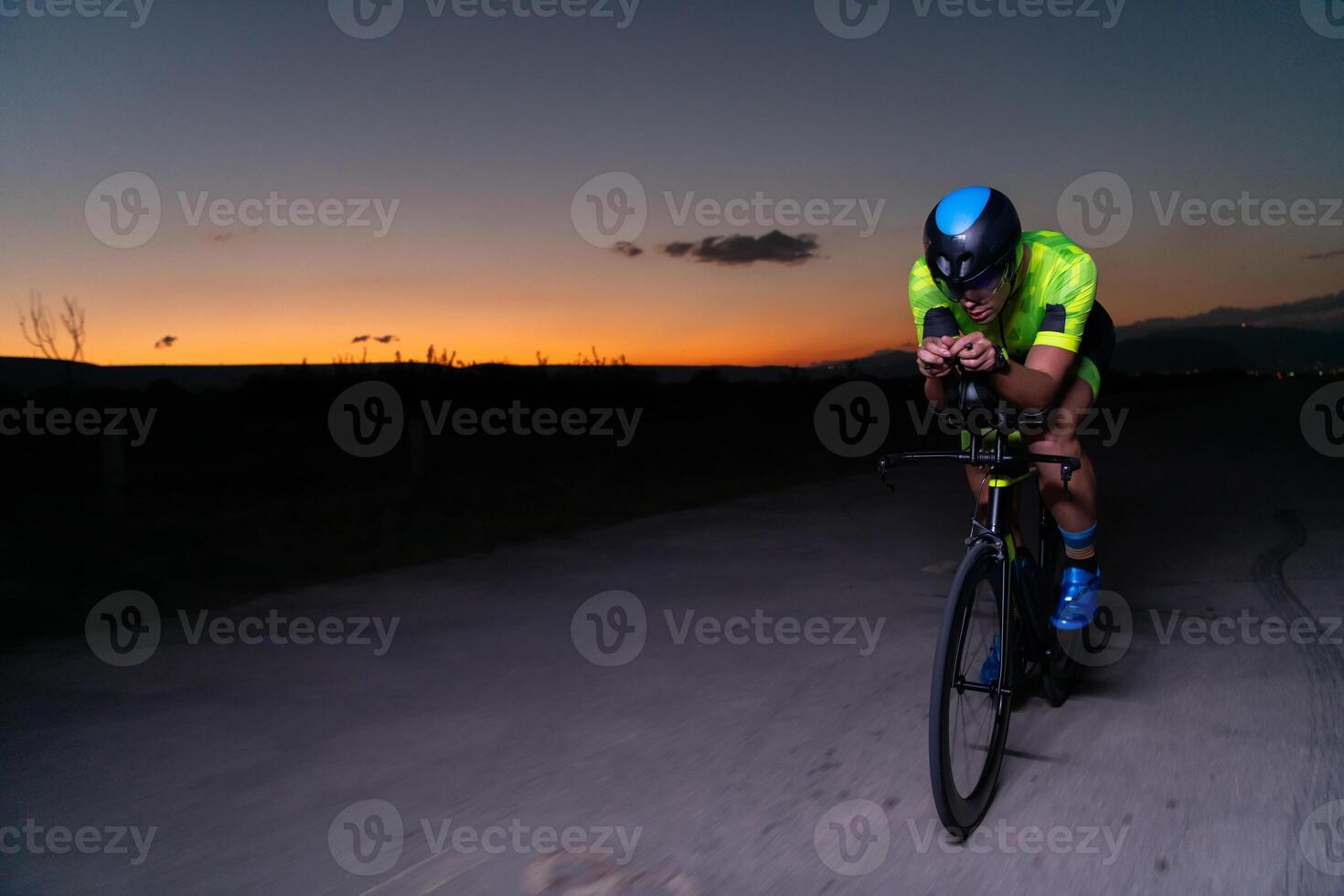 A triathlete rides his bike in the darkness of night, pushing himself to prepare for a marathon. The contrast between the darkness and the light of his bike creates a sense of drama and highlights the photo