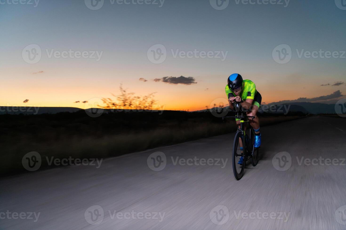 A triathlete rides his bike in the darkness of night, pushing himself to prepare for a marathon. The contrast between the darkness and the light of his bike creates a sense of drama and highlights the photo